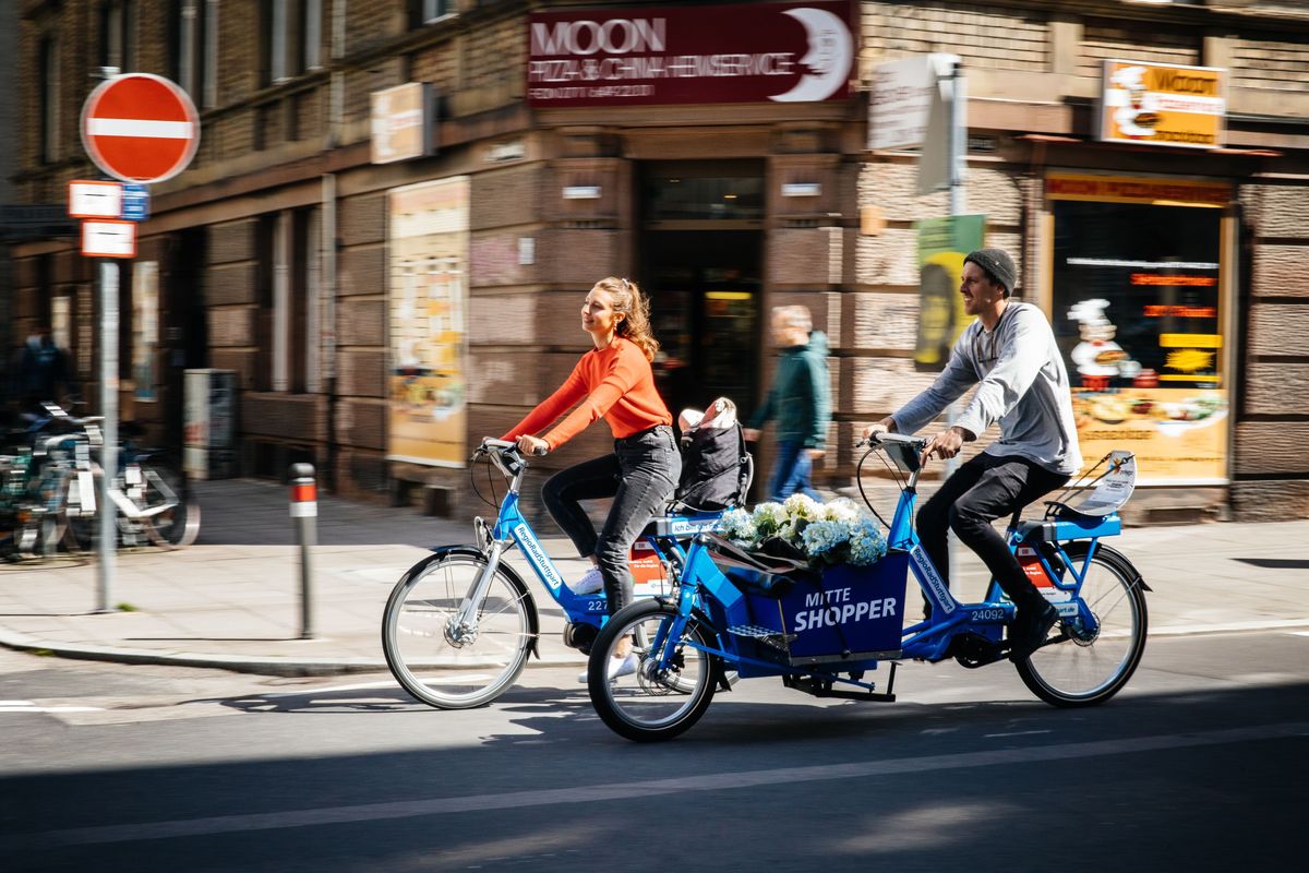 Pärchen auf Lastenrad und Fahrrad fahren durch eine Innenstadt