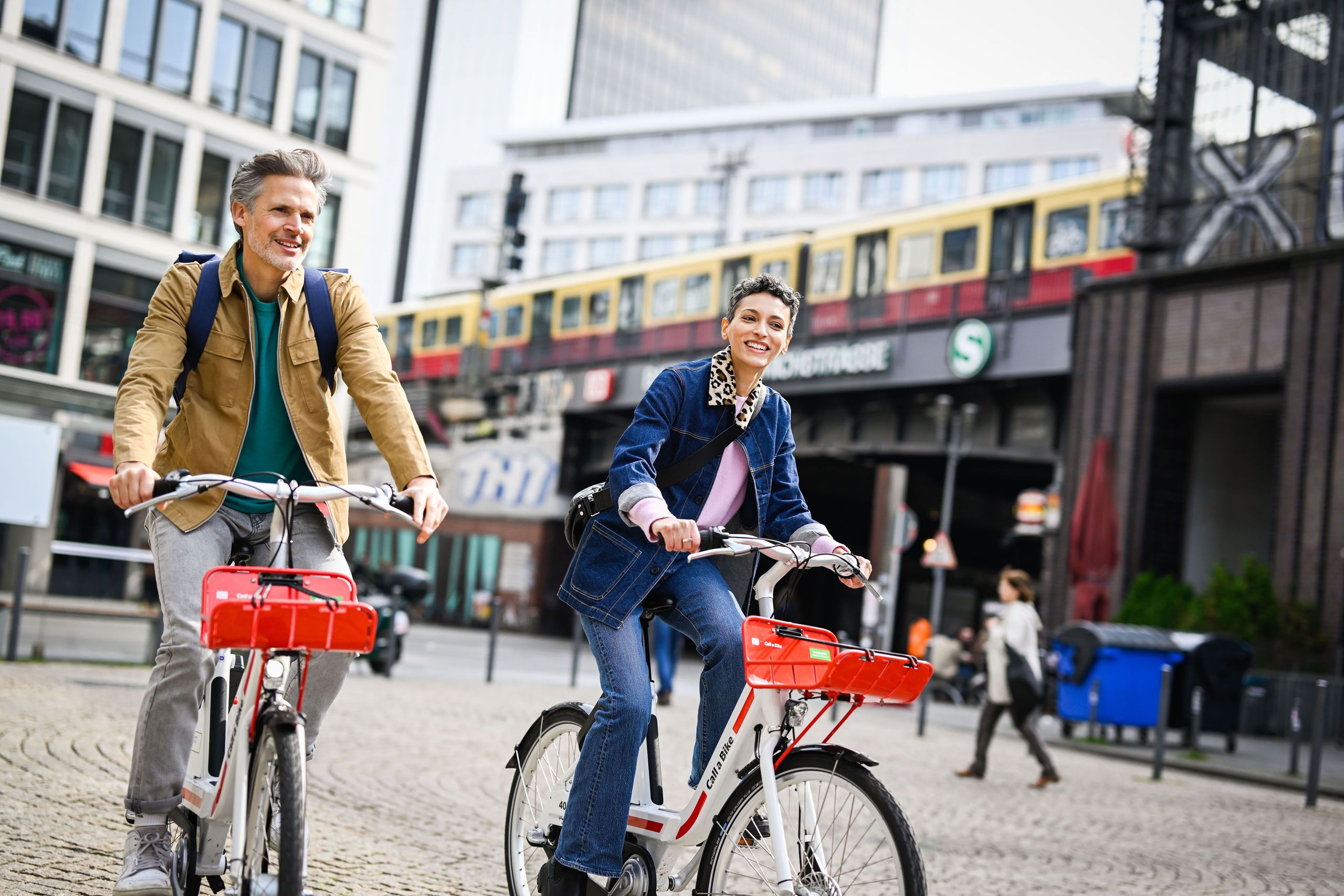 Zwei Menschen fahren mit zwei Bikes an einer S-Bahn-Station in Berlin vorbei
