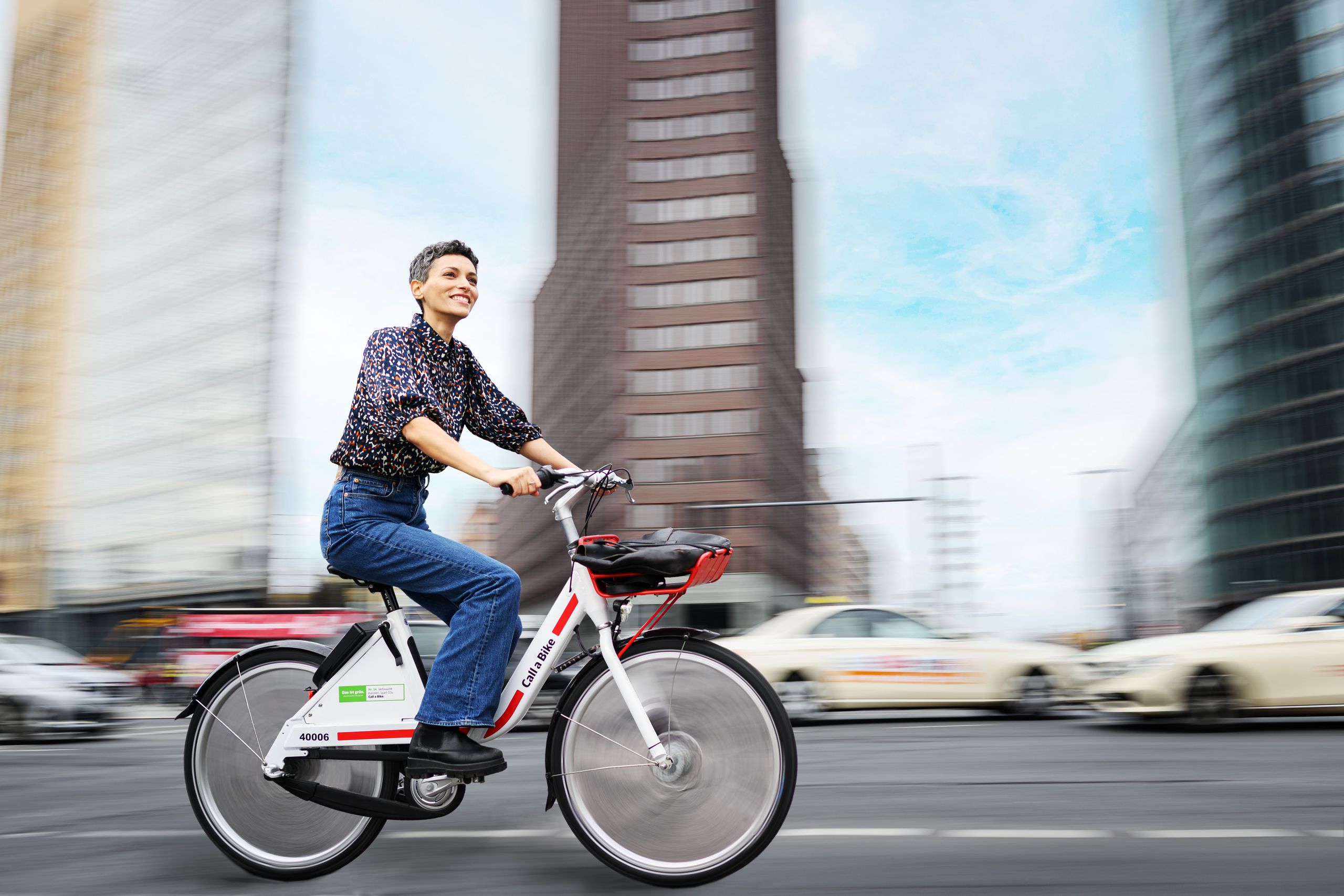 Eine Frau radelt auf einem Call a Bike an Hochhäusern vorbei